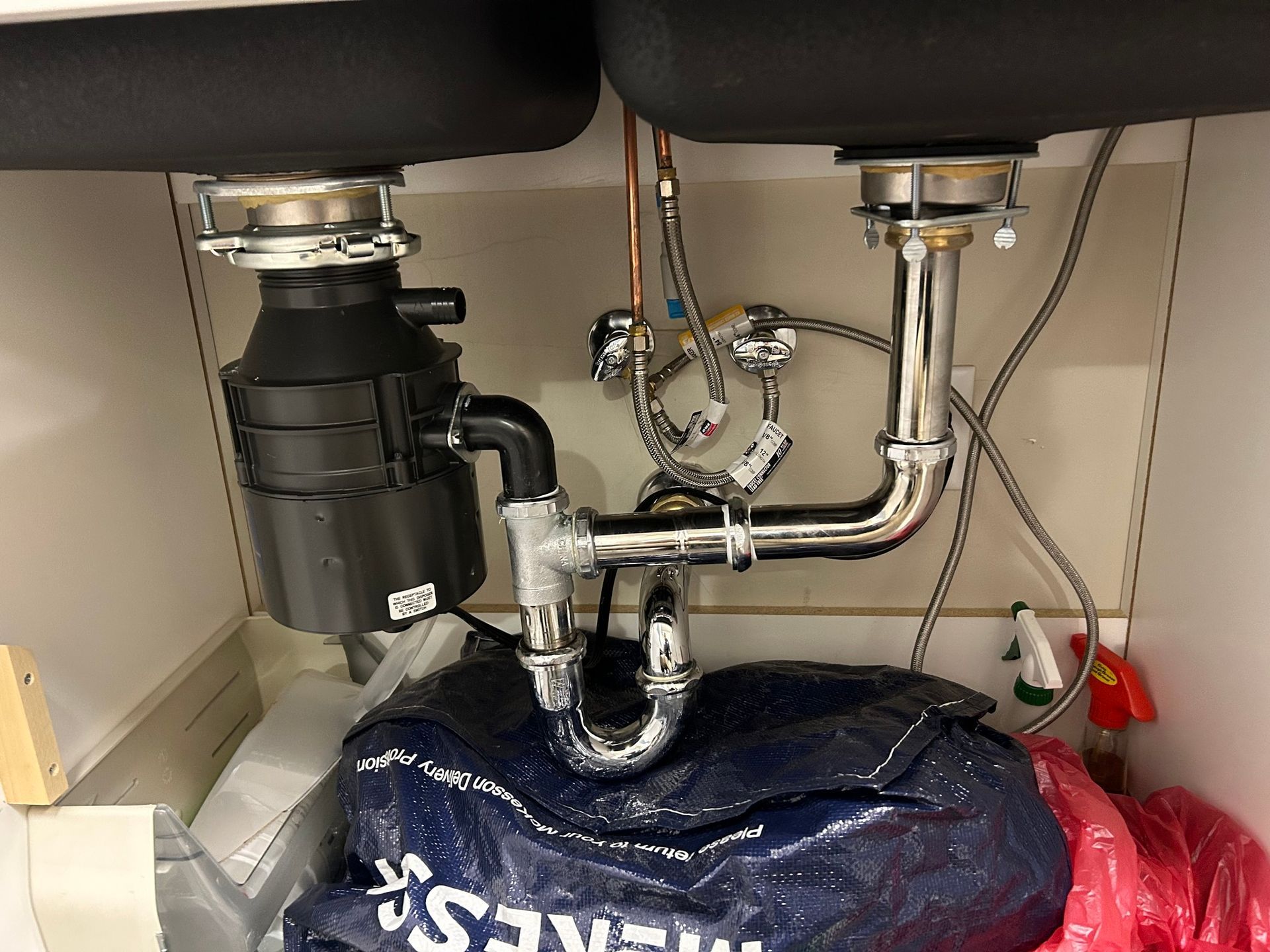Under-sink plumbing with garbage disposal and blue drain cover beneath a kitchen sink