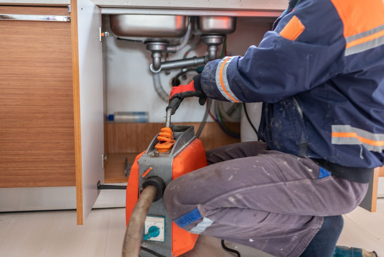 Plumber in blue workwear fixing under-sink pipes with orange tools in a kitchen cabinet