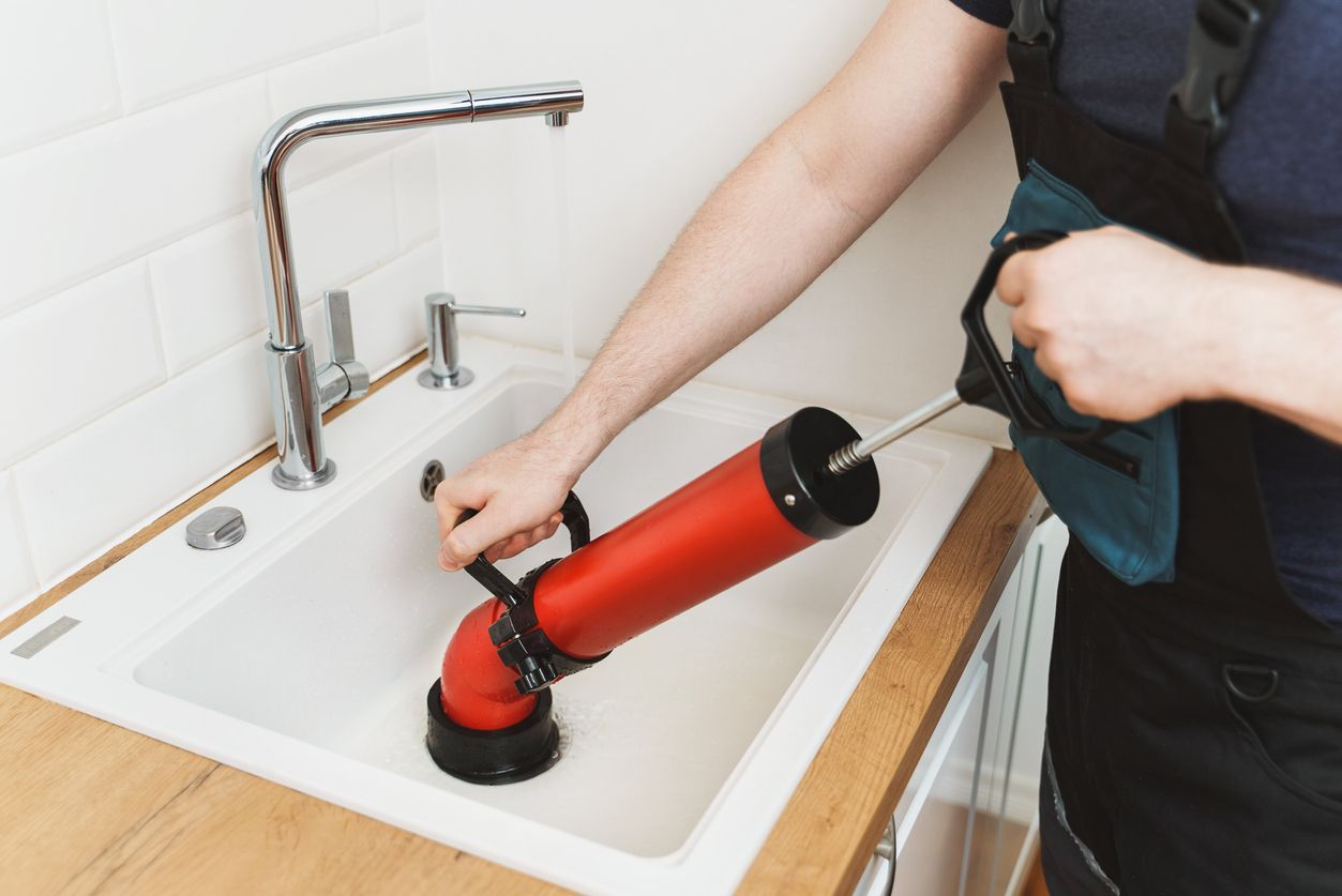 Plumber using a red drain snake to unclog a kitchen sink
