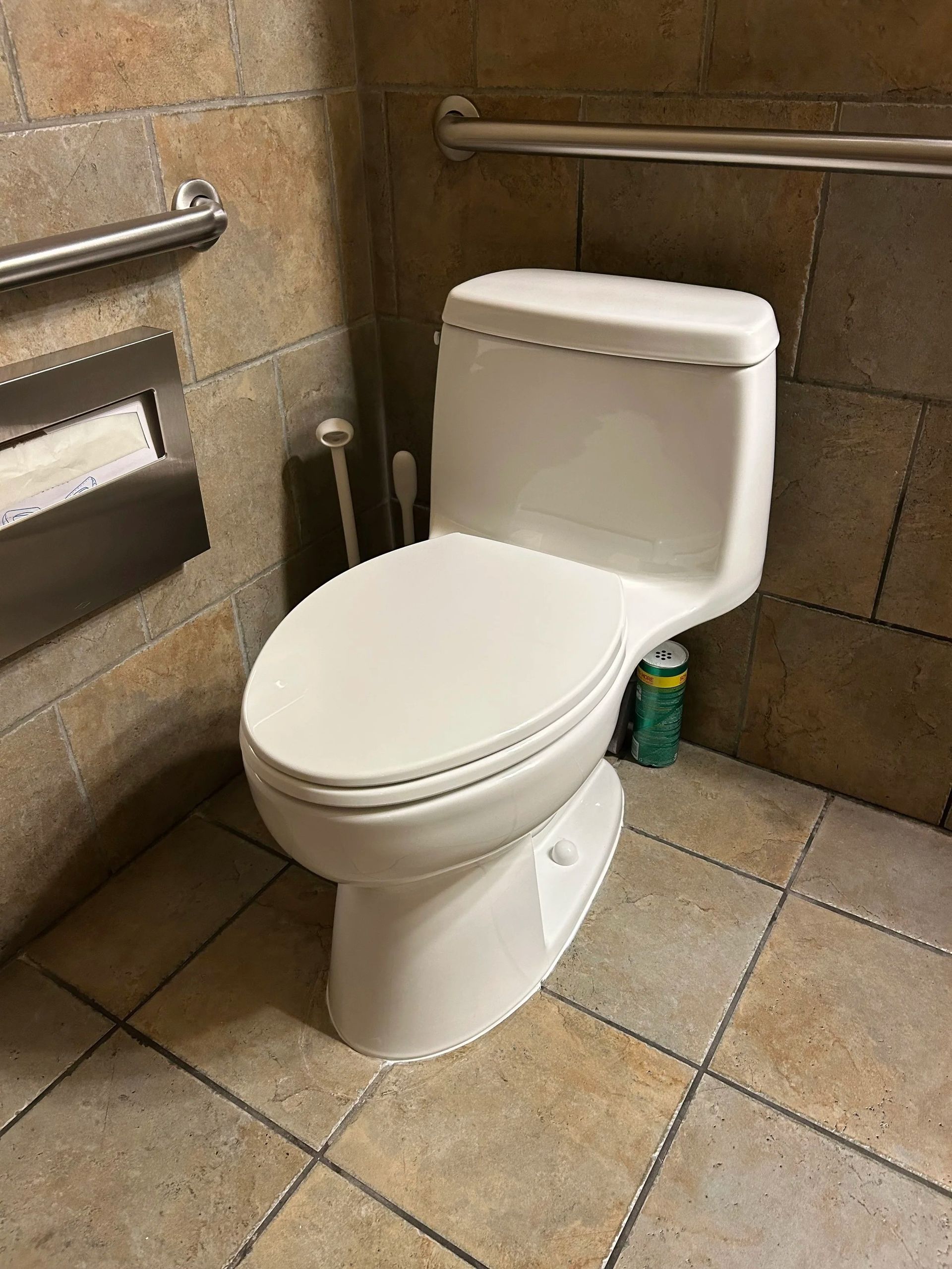 White toilet in a tiled accessible restroom with grab bars and a trash can beside it