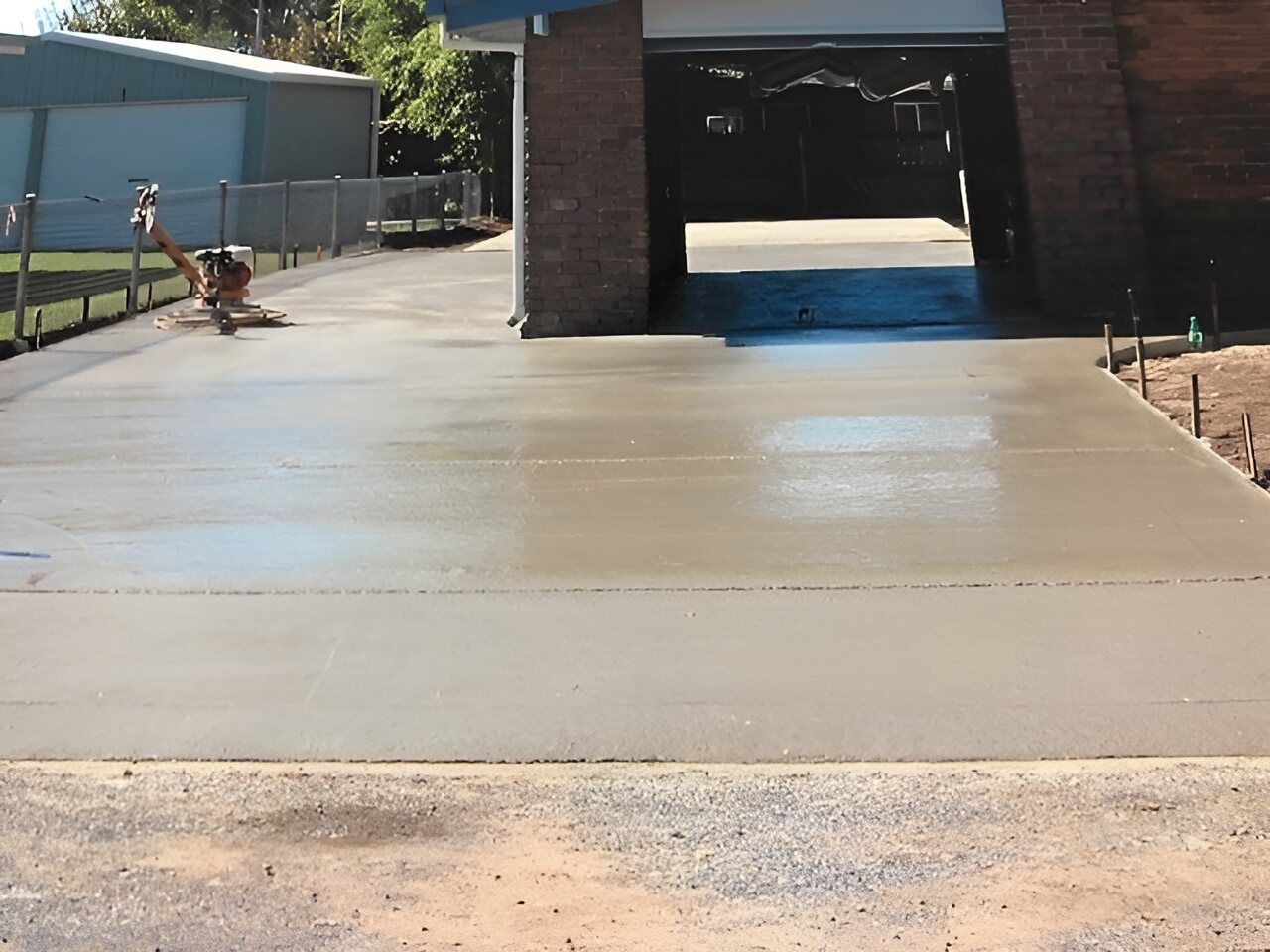 A Concrete Driveway With A Brick Building In The Background — Flash Concreting Pty Ltd In Nindaroo, QLD