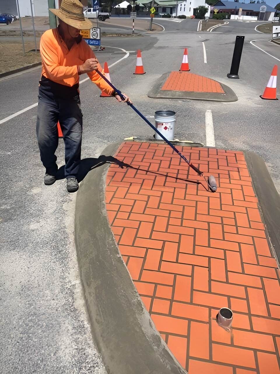A Man Is Painting A Brick Walkway On The Side Of The Road — Flash Concreting Pty Ltd In Nindaroo, QLD