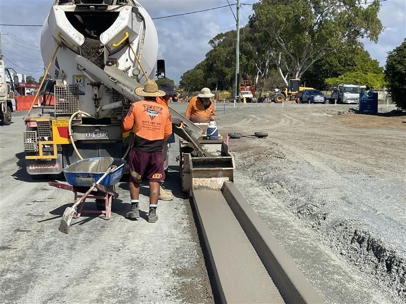 Construction workers pouring concrete along a roadside curb beside a cement mixer. — Flash Concreting Pty Ltd In Nindaroo, QLD
