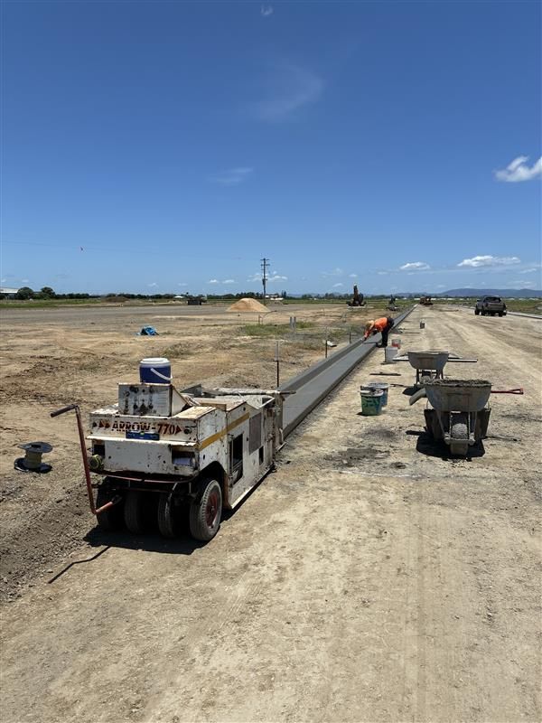 Construction trucks moving a long concrete beam along a dirt road under a clear blue sky — Flash Concreting Pty Ltd In Nindaroo, QLD