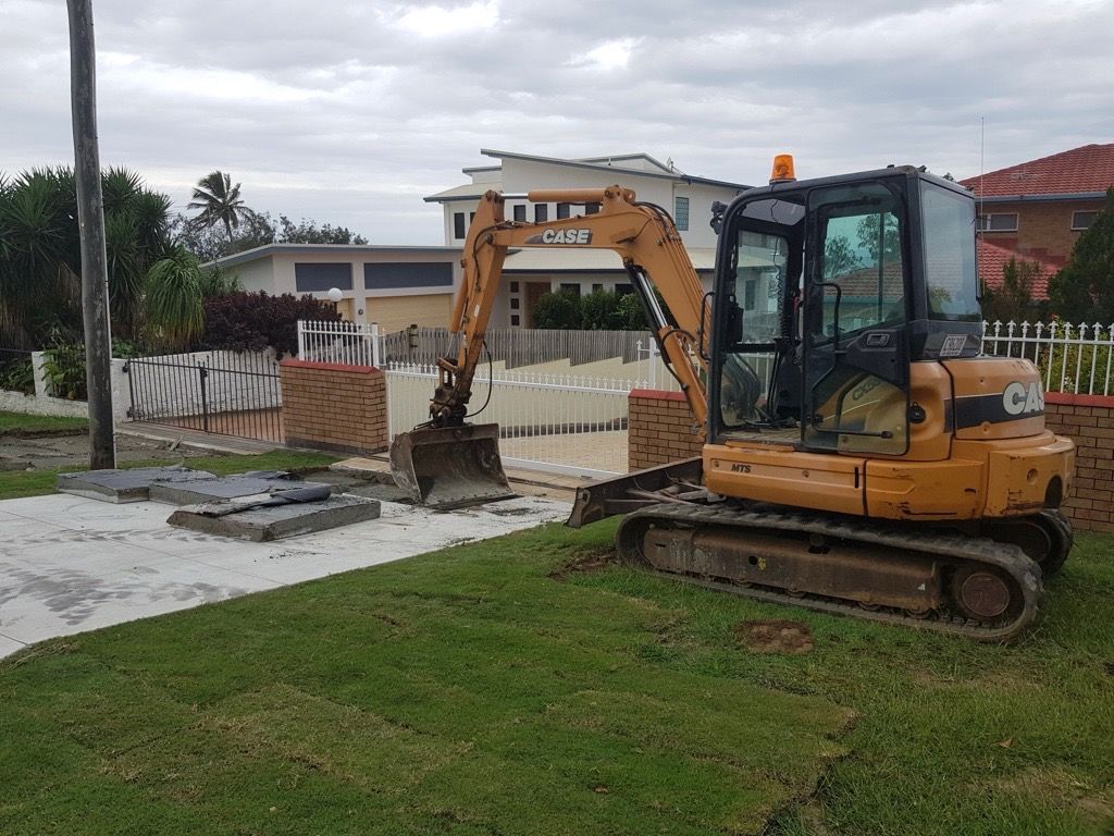 Yellow excavator digging near a fenced residential yard beside a grassy lawn — Flash Concreting Pty Ltd In Nindaroo, QLD
