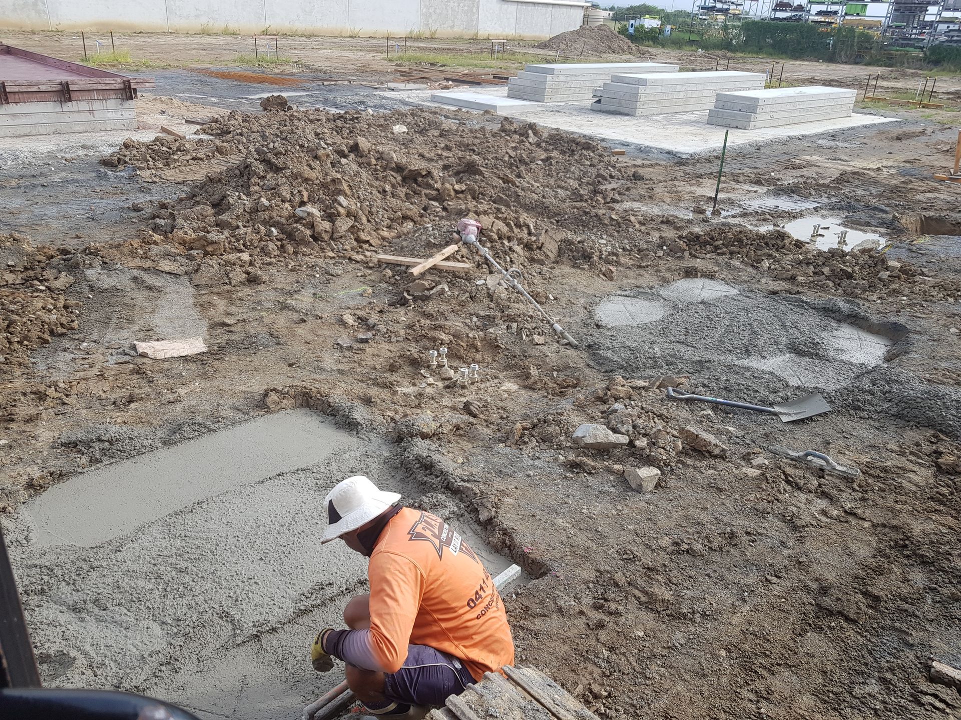 Worker in an orange shirt crouches at a muddy construction site with poured concrete slabs. — Flash Concreting Pty Ltd In Nindaroo, QLD