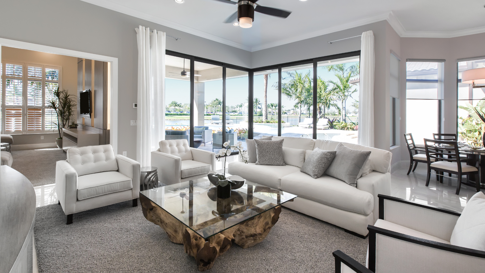 Bright modern living room with white sofas, glass coffee table, and large windows overlooking the water