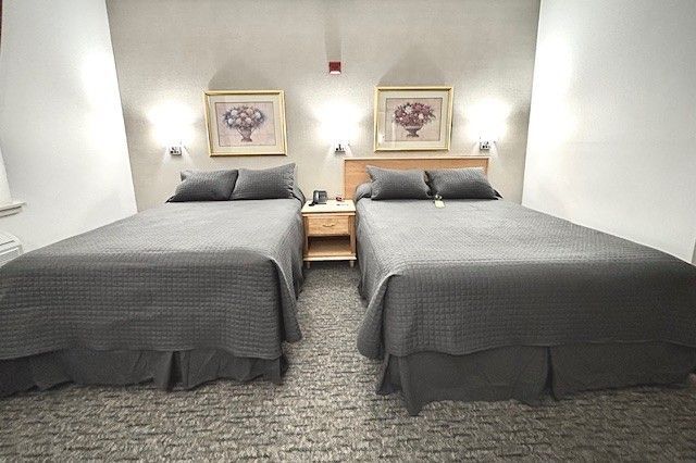 Two twin beds with gray covers and pillows in a room with artwork and a nightstand.
