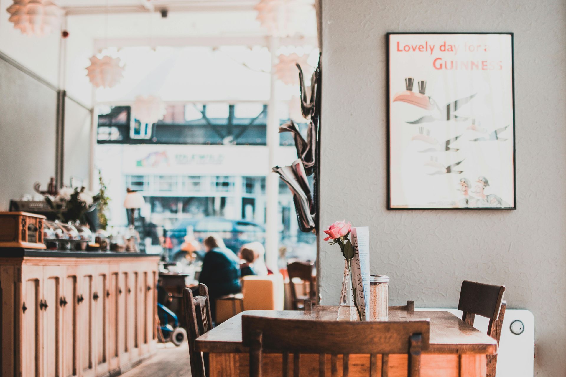 Cafe interior: wooden tables and chairs, poster on a gray wall, large window with people outside.