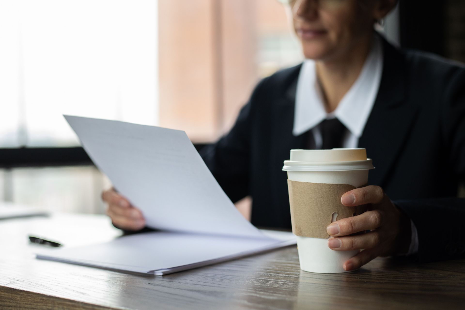 Person holding a coffee cup and reviewing papers at a desk in a bright office