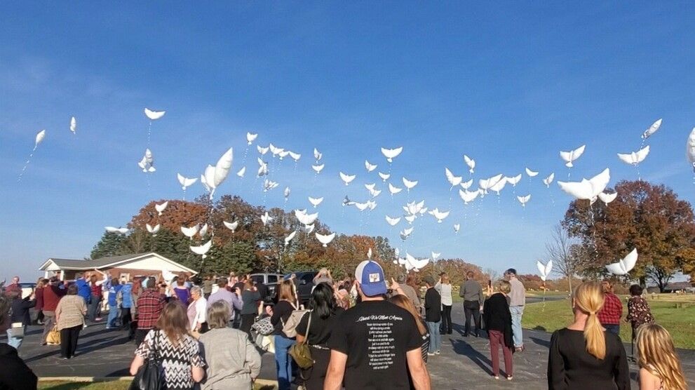 People gathered outdoors releasing white birds into a blue sky at a park event