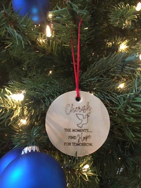 Close-up of a Christmas tree with warm lights and a round ornament reading “Cherish the moments…”