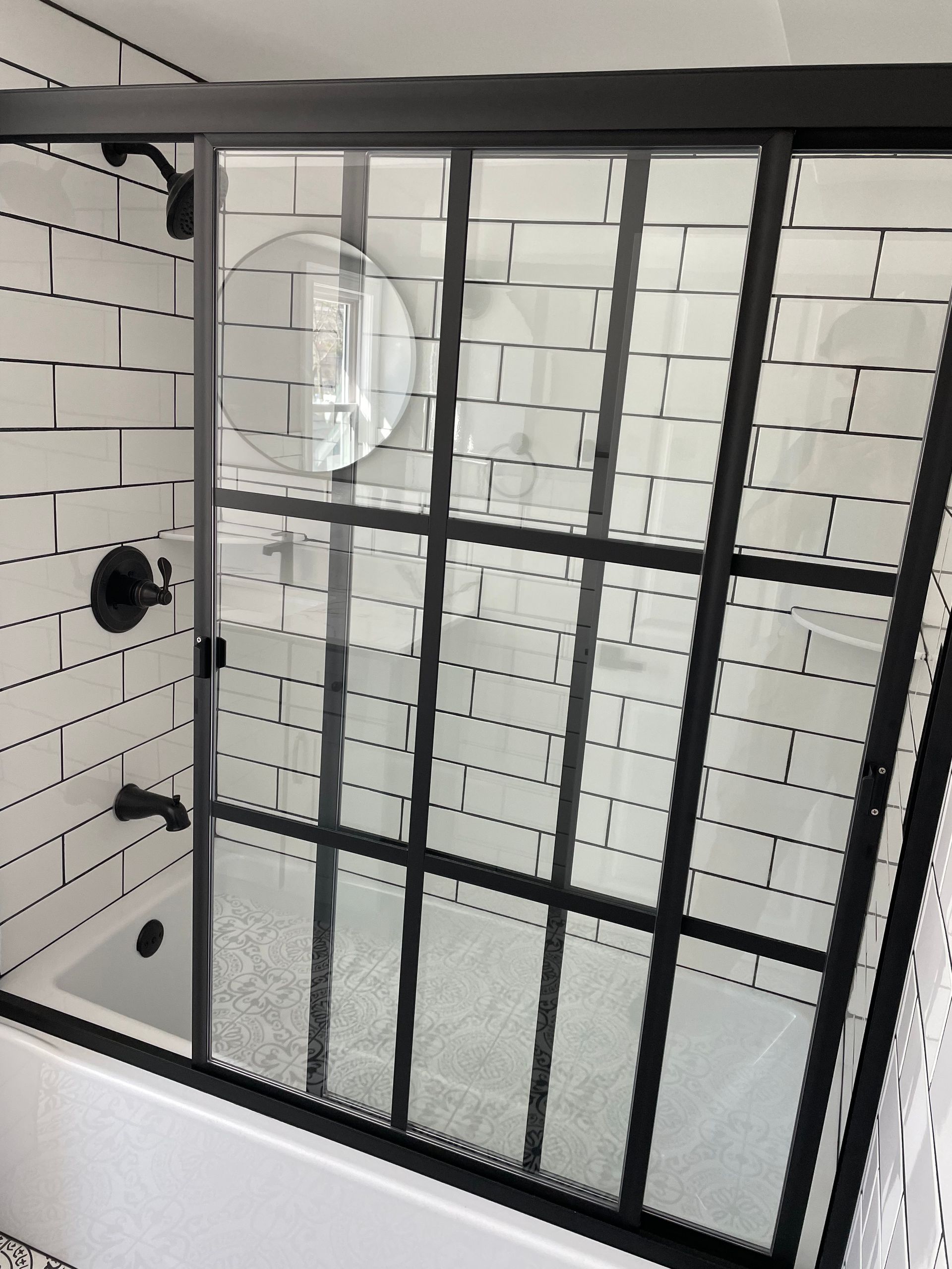Aqua Plumbing Pros | A bathroom with white tiles and a black shower door
