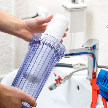 Aqua Plumbing Pros | A person is holding a clear container in front of a sink