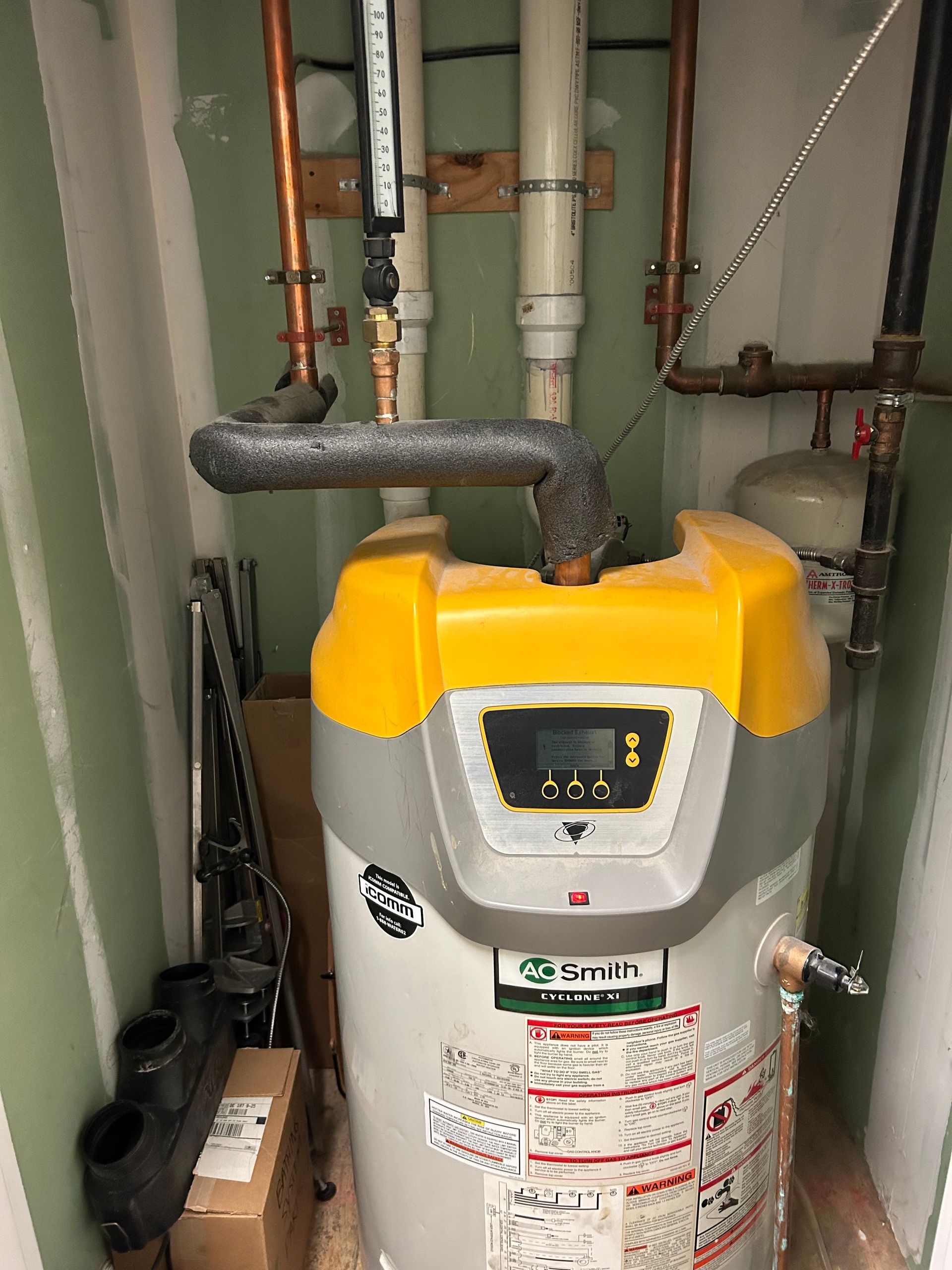 Aqua Plumbing Pros | A yellow and gray water heater is sitting in a corner of a room.