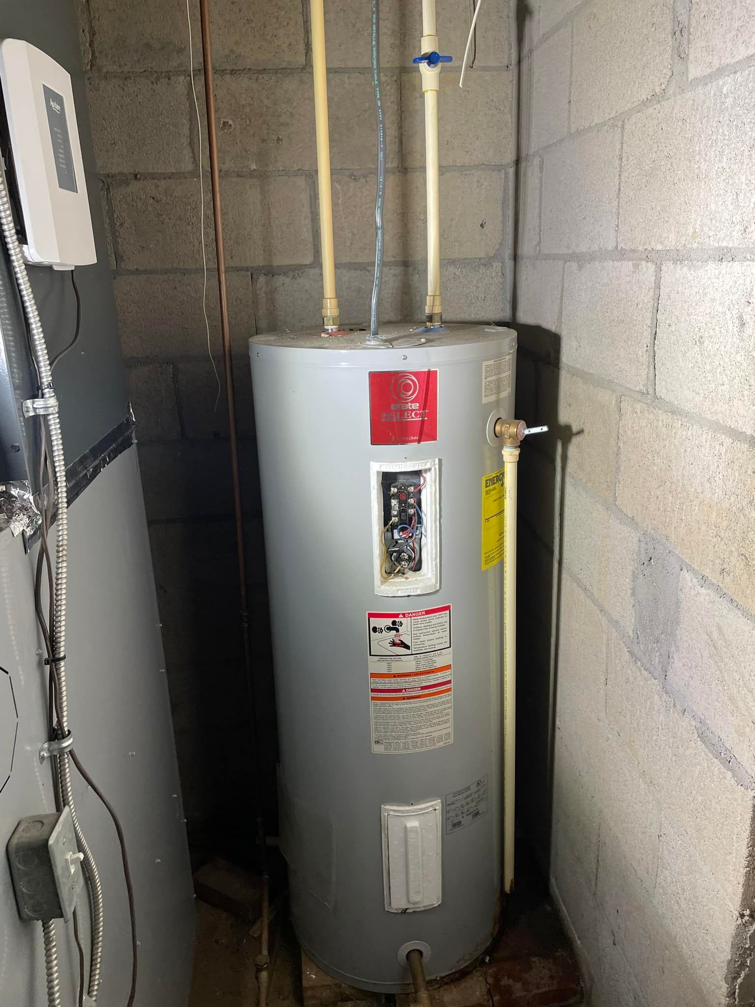 Aqua Plumbing Pros | A water heater is sitting in a corner of a room next to a brick wall.