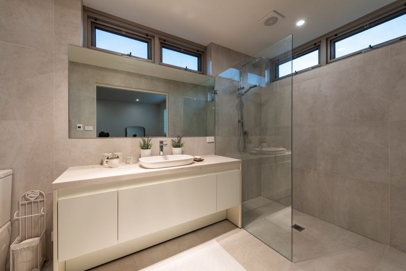 A bathroom with a walk in shower , sink , mirror and toilet.
