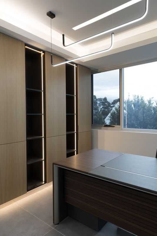 A room with a desk , shelves , and a large window.