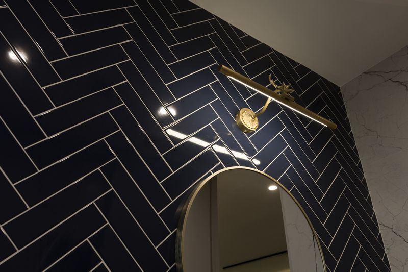 A bathroom with dark blue tiles and a mirror