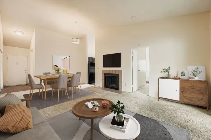 Open-plan living and dining room with beige decor, fireplace, TV, and wooden table set for six.