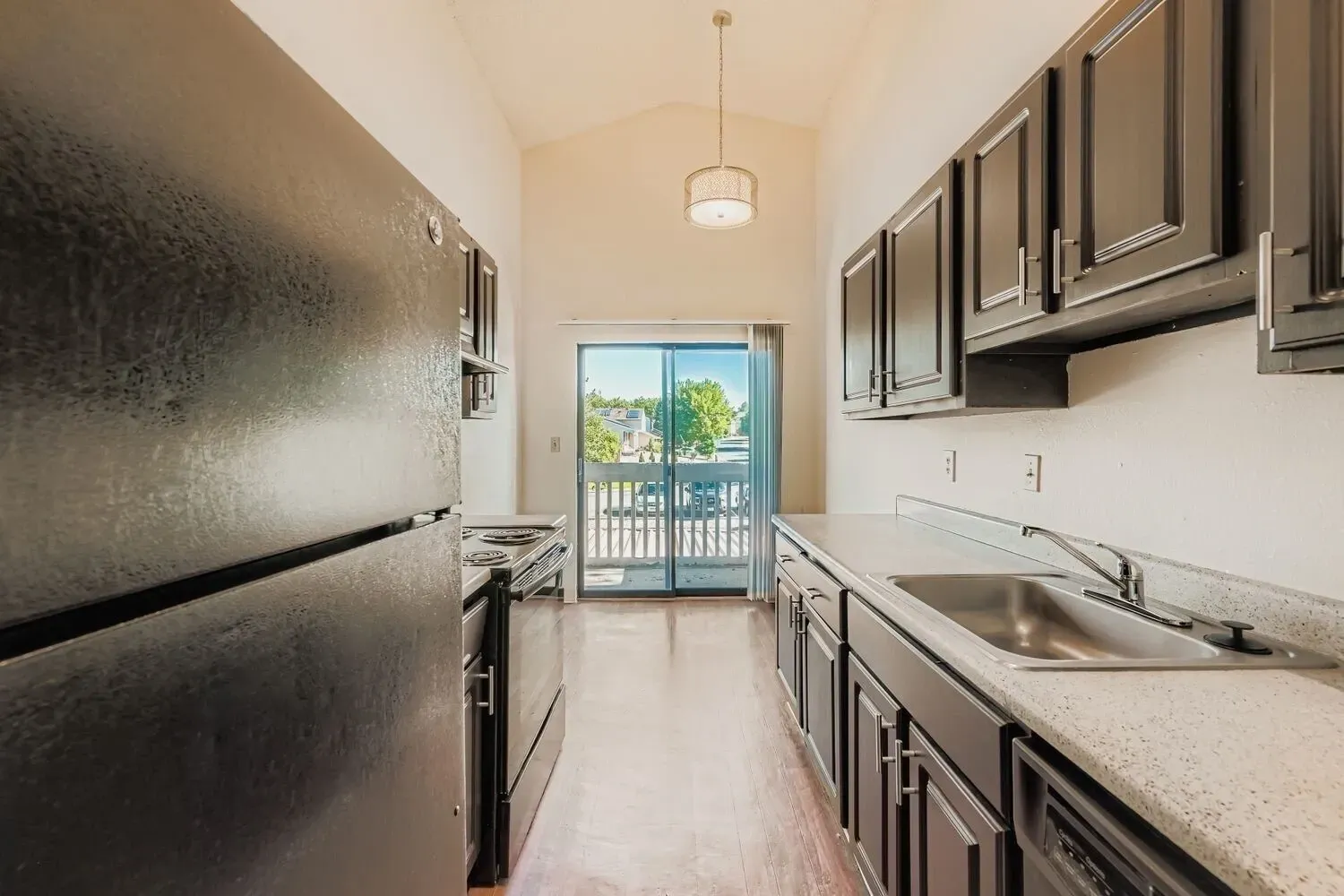 Kitchen with dark cabinets, stainless steel sink, black refrigerator, and stove.