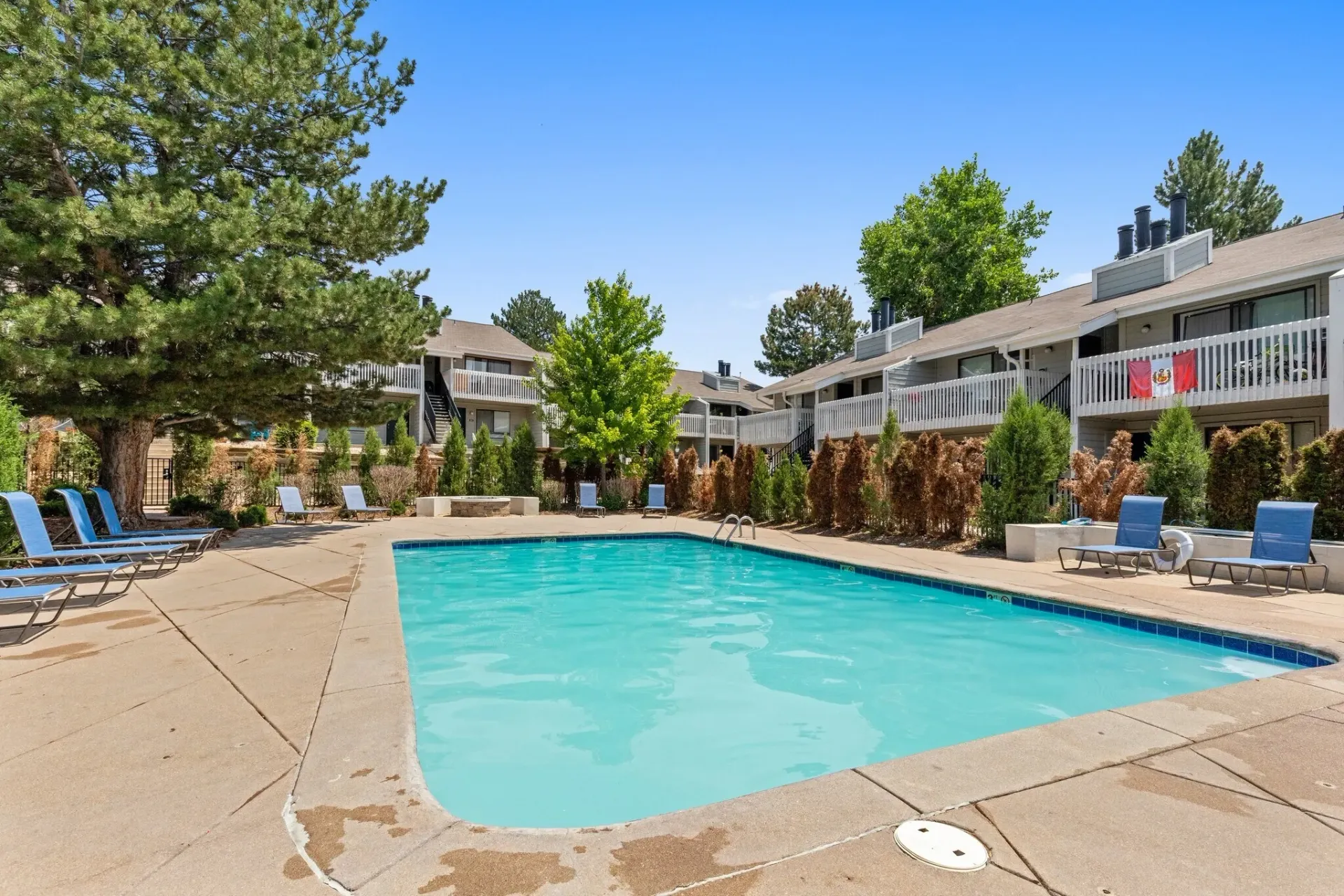 Resort-style swimming pool with lounge chairs and apartment buildings in the background.
