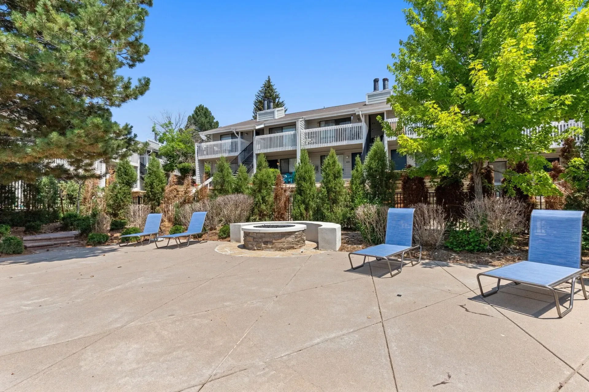 Outdoor lounge area with fire pit and lounge chairs in front of apartment buildings.