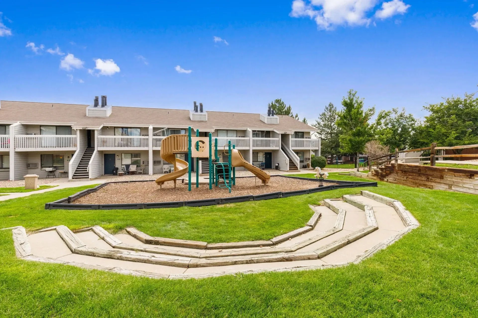 Apartment building exterior with playground and tiered seating area.