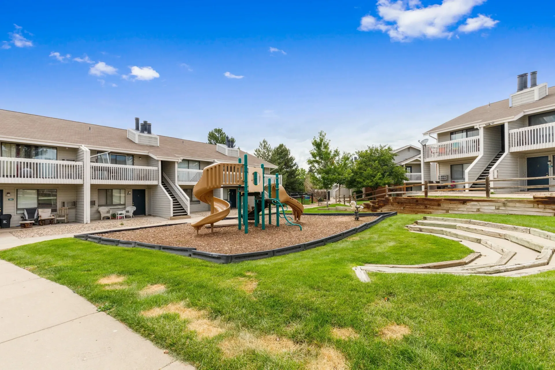 Apartment courtyard with playground, tan walkways, green lawn, and blue sky