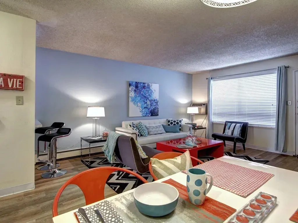Bright living room with sofa, lamps, table, chairs, and a large window with blinds