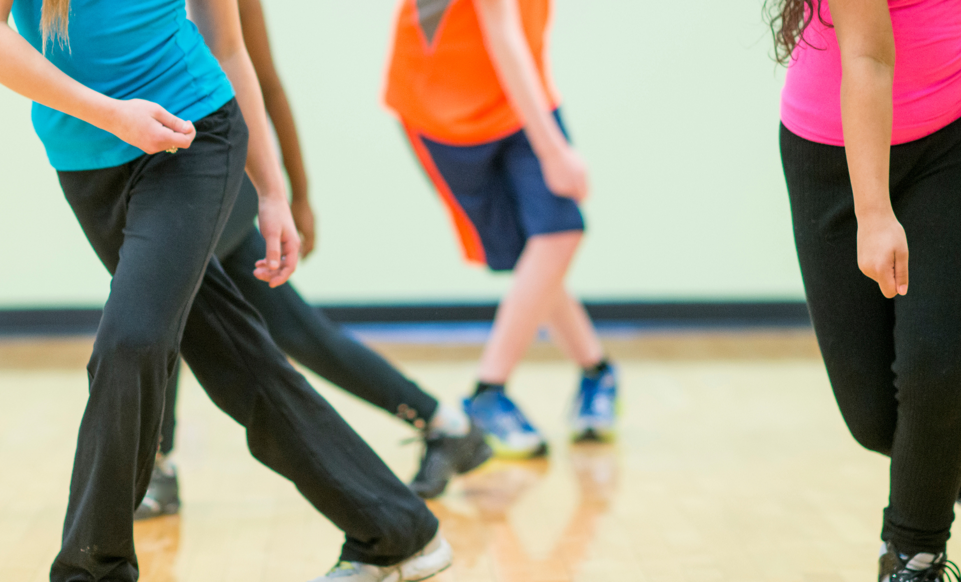 People exercising in a dance or fitness class, wearing colorful tops and black pants.