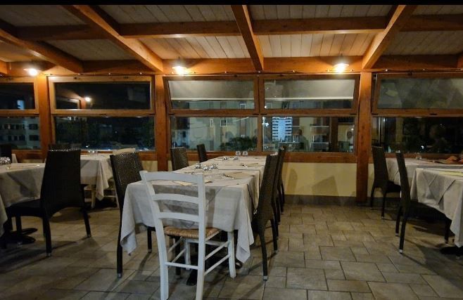 Sala da pranzo vuota di un ristorante con tovaglie bianche, travi in legno e grandi finestre, di notte.
