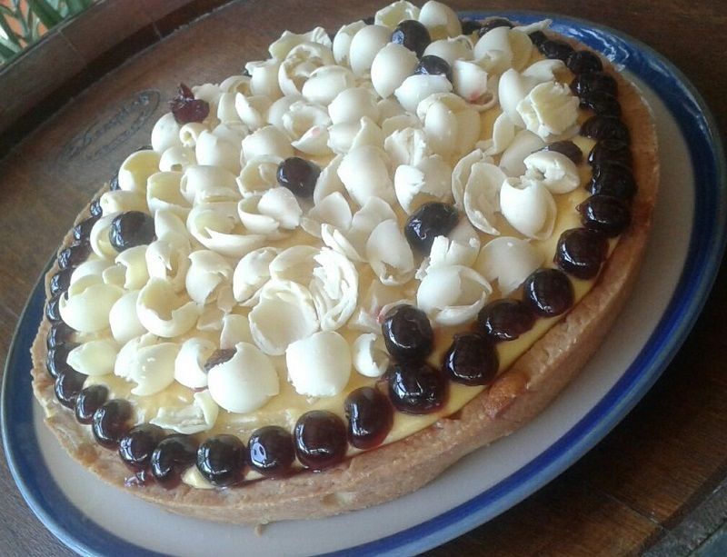 Torta rotonda da dessert con ciuffi di crema bianca e ciliegie nere, servita su un piatto.