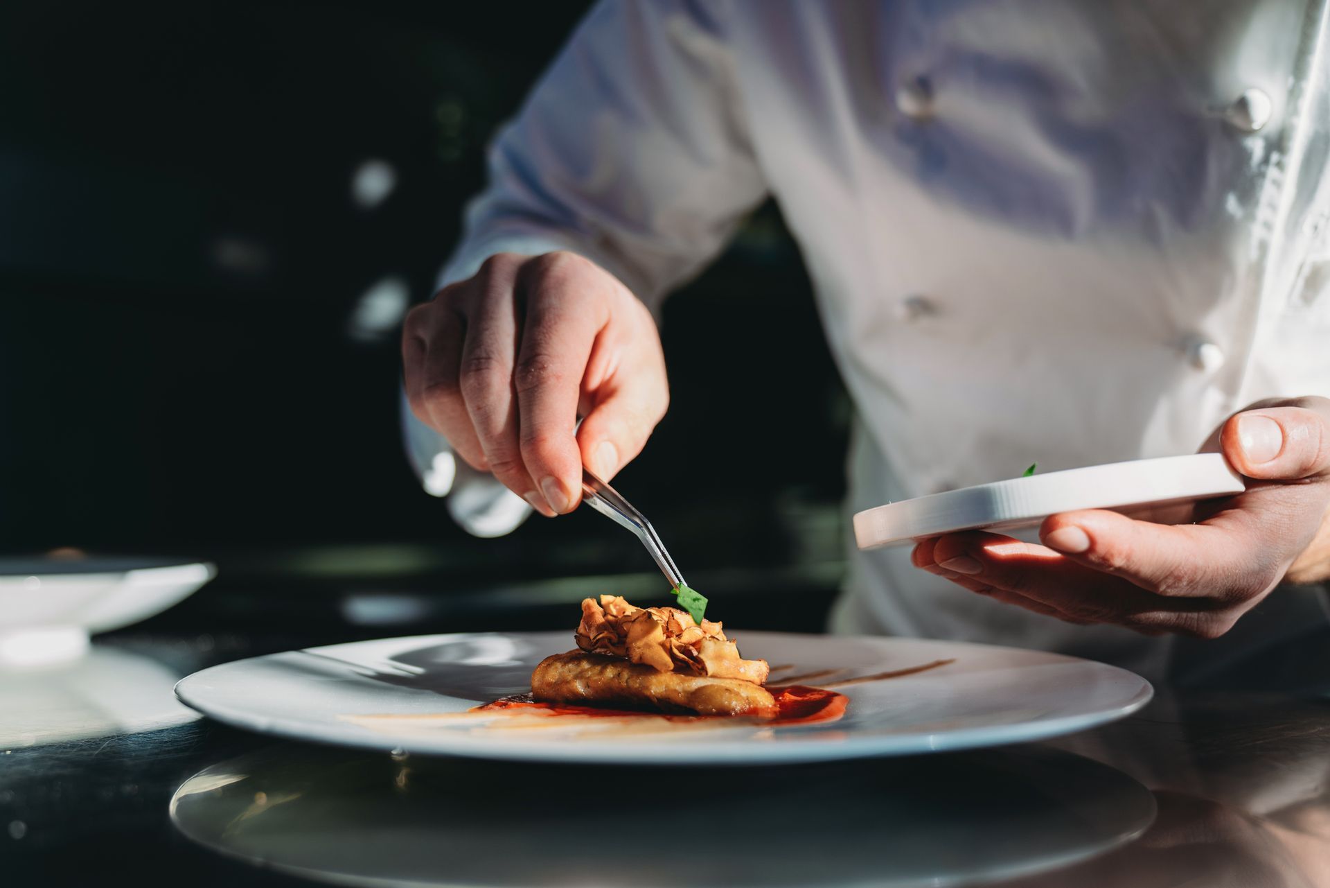 In una cucina buia, lo chef impiatta una pietanza gourmet su un piatto bianco con un cucchiaio.