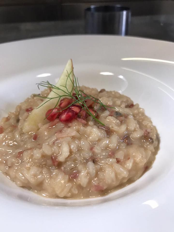 Risotto cremoso in una ciotola bianca, guarnito con semi di melograno e rametti di aneto.