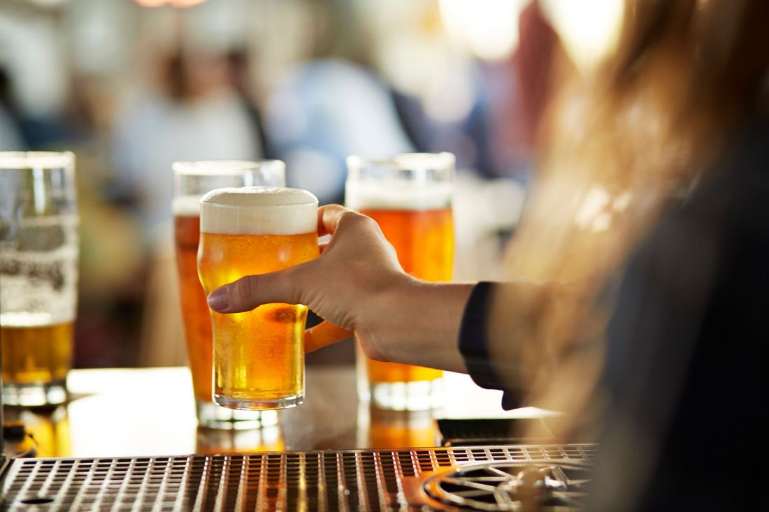 Una mano si allunga per prendere un bicchiere di birra dal bancone di un bar, con diverse birre sullo sfondo.