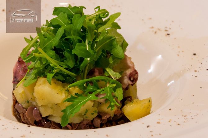 Insalata verde su un piatto bianco, con tartare di manzo, cubetti di patate ed erbe aromatiche.