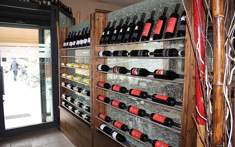 Bottiglie di vino esposte su scaffali a muro in una piccola enoteca accanto a una porta a vetri.