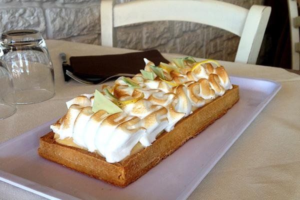 Torta rettangolare con panna montata e meringa tostata su un piatto bianco al tavolino di un caffè.
