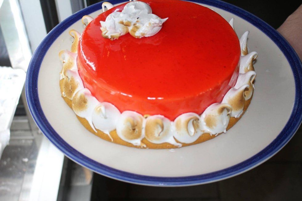 Torta glassata di rosso con decorazioni di crema bianca su un piatto con bordo blu.
