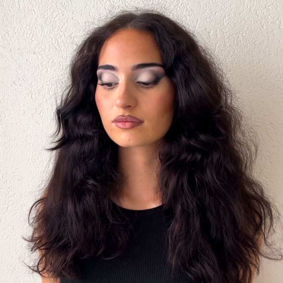 Eine Frau mit langen dunklen Haaren trägt ein schwarzes Hemd und hat die Augen geschlossen.