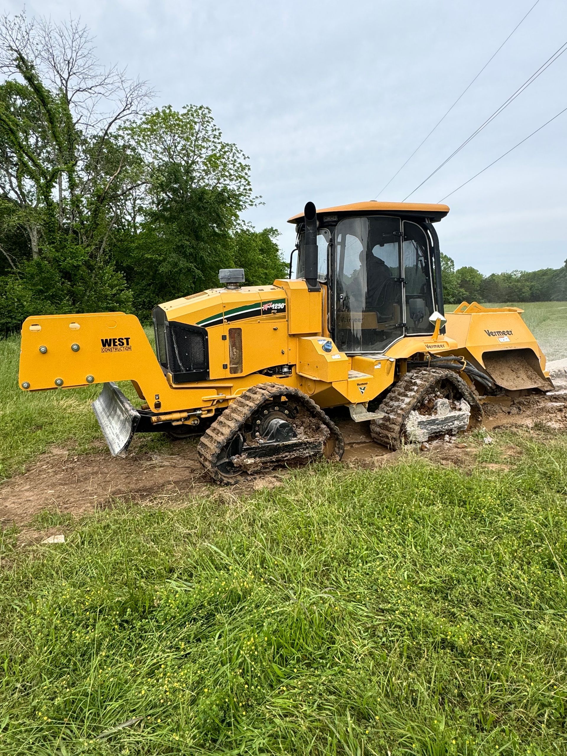 Yellow tracked vehicle stuck in mud, clearing brush in a field. Cloudy sky.