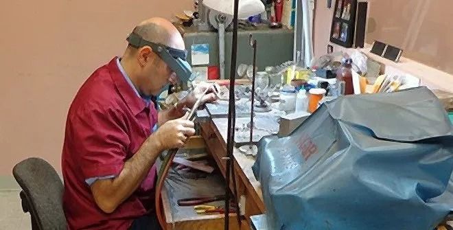 Person crafting jewelry at a workbench with tools and a small piece in progress