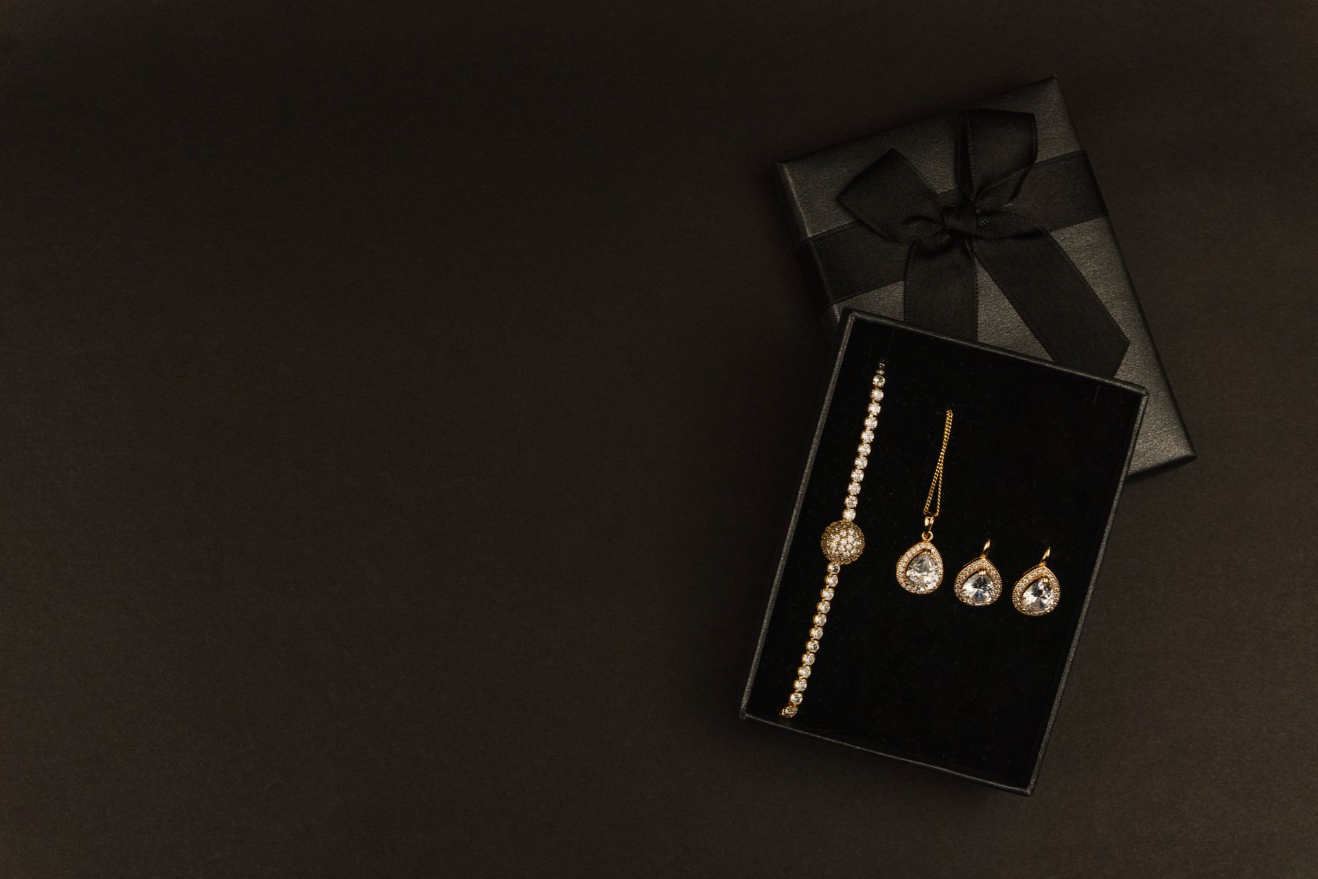 Black gift box with dangling gold earrings and a bracelet on a dark background