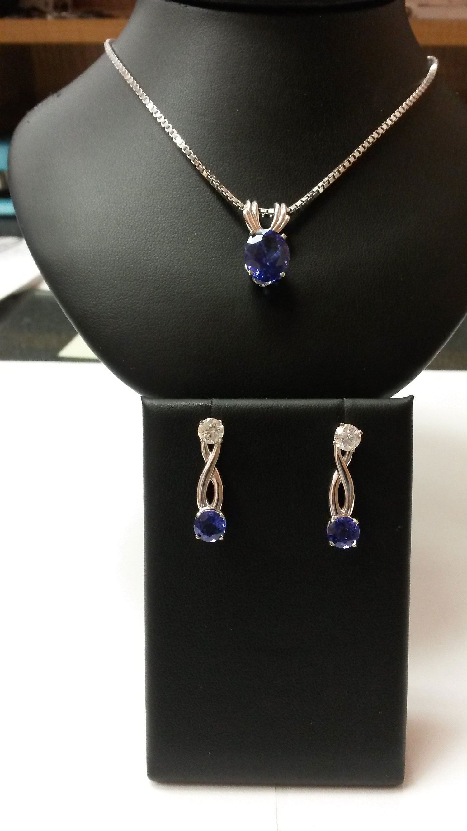 Silver necklace and matching earrings with blue gemstones displayed on black stands.