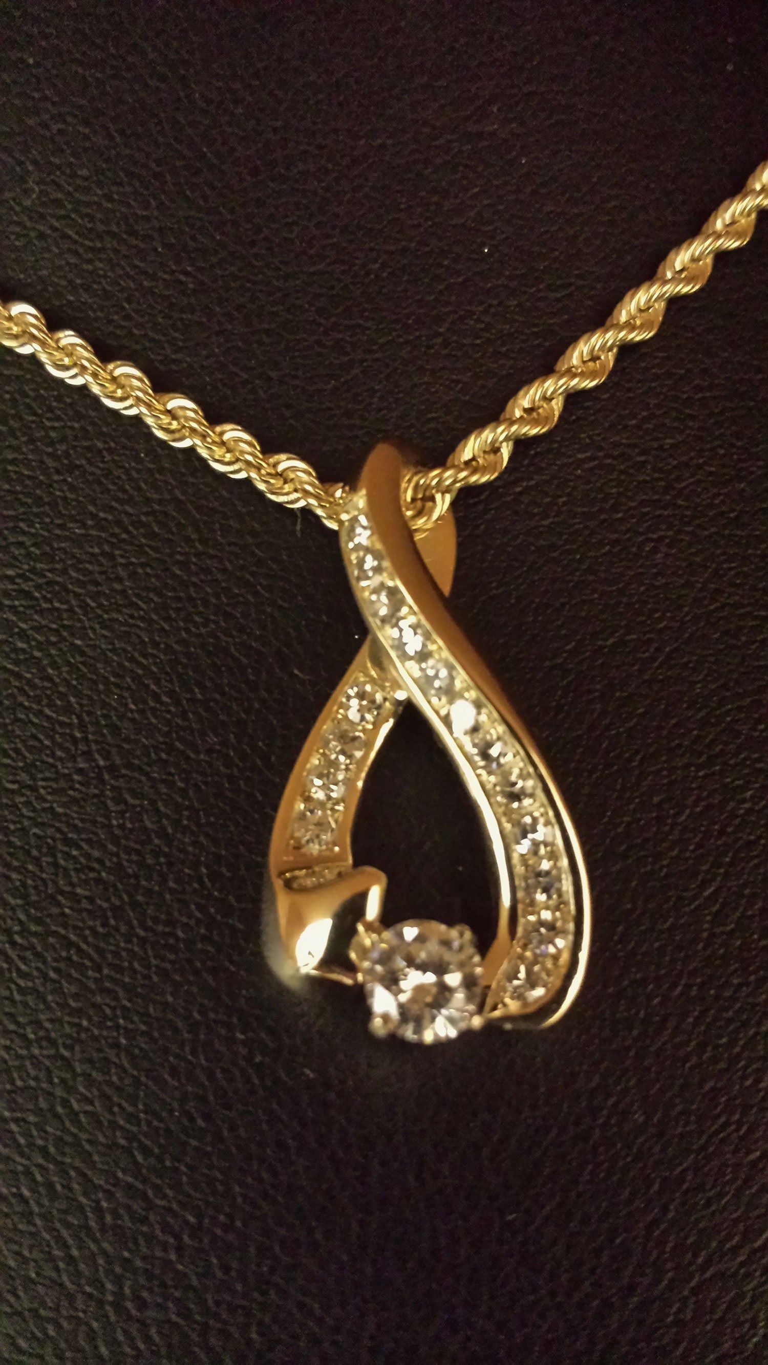 Gold pendant necklace with a teardrop design and small sparkling stones on a dark background