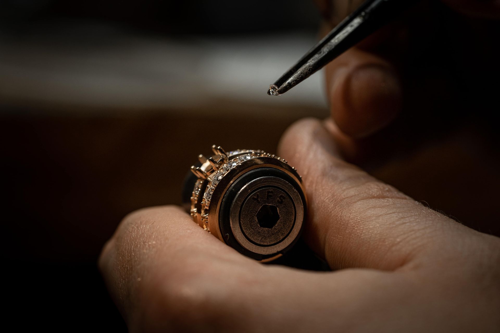 Close-up of a person adjusting a gold watch with a tool in a dim workshop