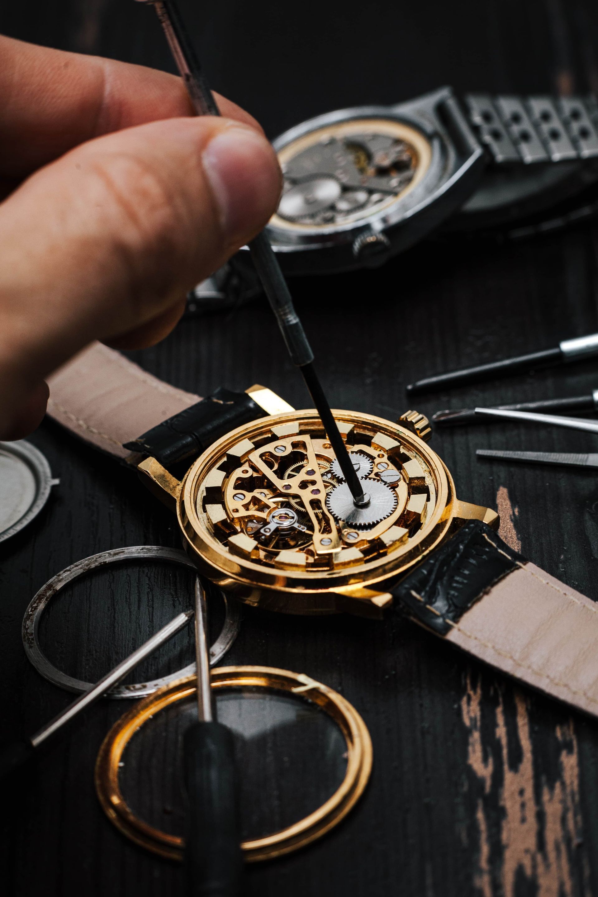 Watchmaker repairing a gold skeleton watch on a dark workbench with tools nearby