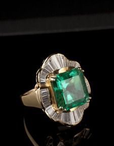 Gold ring with a large square green gemstone and fluted clear side stones on a black background
