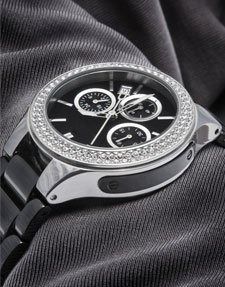 Black luxury chronograph watch with diamond bezel on textured gray fabric